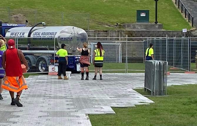 Tapped Out water tanker supplying an event site, with crew filling containers beside the temporary fencing and trackway