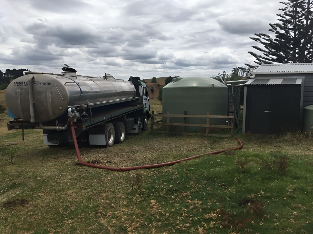 Tapped Out water tanker truck connected to a large green storage tank at a rural property